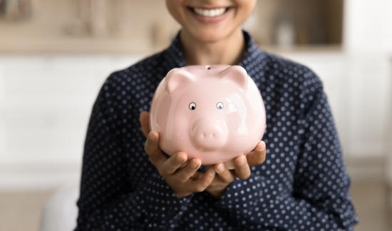 Smiling female student holding a piggy bank.