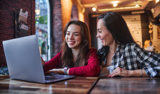 Mother and daughter smiling while using the laptop together.
